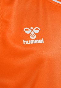 Orange idrottstyg med en vit "hummel"-logotyp och en bi-liknande grafik. Ytan är jämn med en lätt glans.