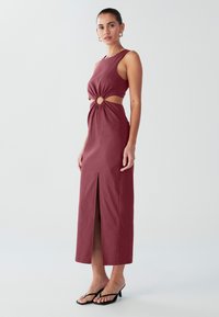 V�ýrazné červené šaty s priliehavým živôtikom, výrezom v páse so štýlovým kruhovým detailom a bočným rozparkom, vyrobené z hladkej látky.