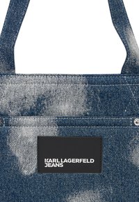 Denim torba s uzorkom u izblijedjeloj plavoj boji, s pravokutnom crnom kožnom etiketom na kojoj je u bijelom utisnut natpis "KARL LAGERFELD JEANS".