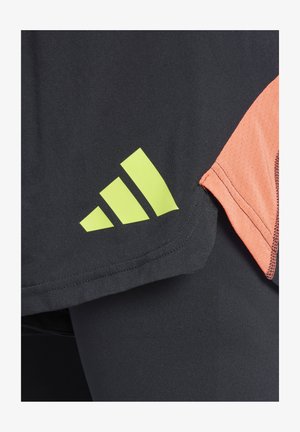 Zwarte sportshirt met oranje mesh accenten; heeft een opvallend groen drie-strepenlogo op de onderste zoom. De textuur lijkt glad te zijn.