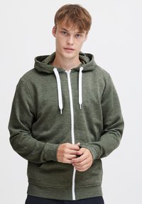 Groene ritssluitende hoodie gemaakt van een zachte, gestructureerde stof. Voorzien van een capuchon, witte trekkoorden en een voorkant met rits. Klassiek casual ontwerp.