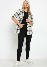 Sort og hvid plaid skjorte med knapper, lange ærmer rullet op, kombineret med sorte tætsiddende bukser og hvide sneakers med beige detaljer.