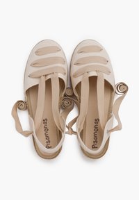 Zapatillas de lona beige claro con punta redonda, que cuentan con cuatro tiras de tela horizontales y detalles de cinta enrollada en el talón.