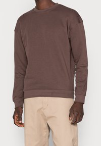 Sudadera marrón de manga larga con puños y dobladillo acanalados; hecha de un tejido suave, presenta un diseño clásico de cuello redondo y un ajuste relajado.