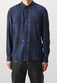 Koszula na guziki z ciemnego, wzorzystego materiału w niebieskie, czarne i turkusowe zawijasy. Długie rękawy i szpiczasty kołnierzyk.