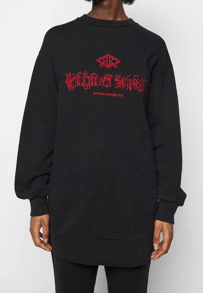 Svart oversized sweatshirt med röd broderad text, med rund halsringning och långa ärmar. Materialet har en jämn och mjuk textur.