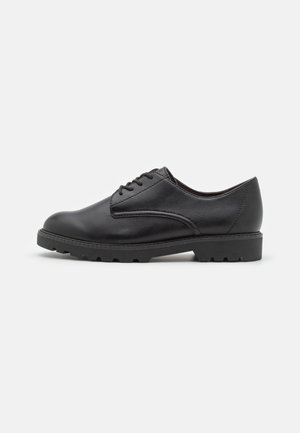 Zapato de cuero negro con puntera redondeada, tacón bajo y diseño de cordones. Presenta una suela texturizada con ranuras para mayor tracción.