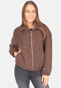 Braune, flauschige Zip-Jacke mit einer strukturierten Oberfläche, elastischen Bündchen und Seitentaschen, kombiniert mit grauen Jeans.