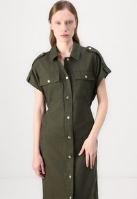 Rochie din in verde, cu mâneci scurte, epauleți la umeri, două buzunare pe piept și închidere frontală cu nasturi. Textură netedă, până la genunchi.