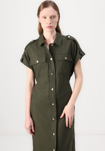 Robe chemise en lin vert avec des manches courtes, épaulettes aux épaules, deux poches poitrine et une fermeture à boutons à l'avant. Texture lisse, longueur genou.