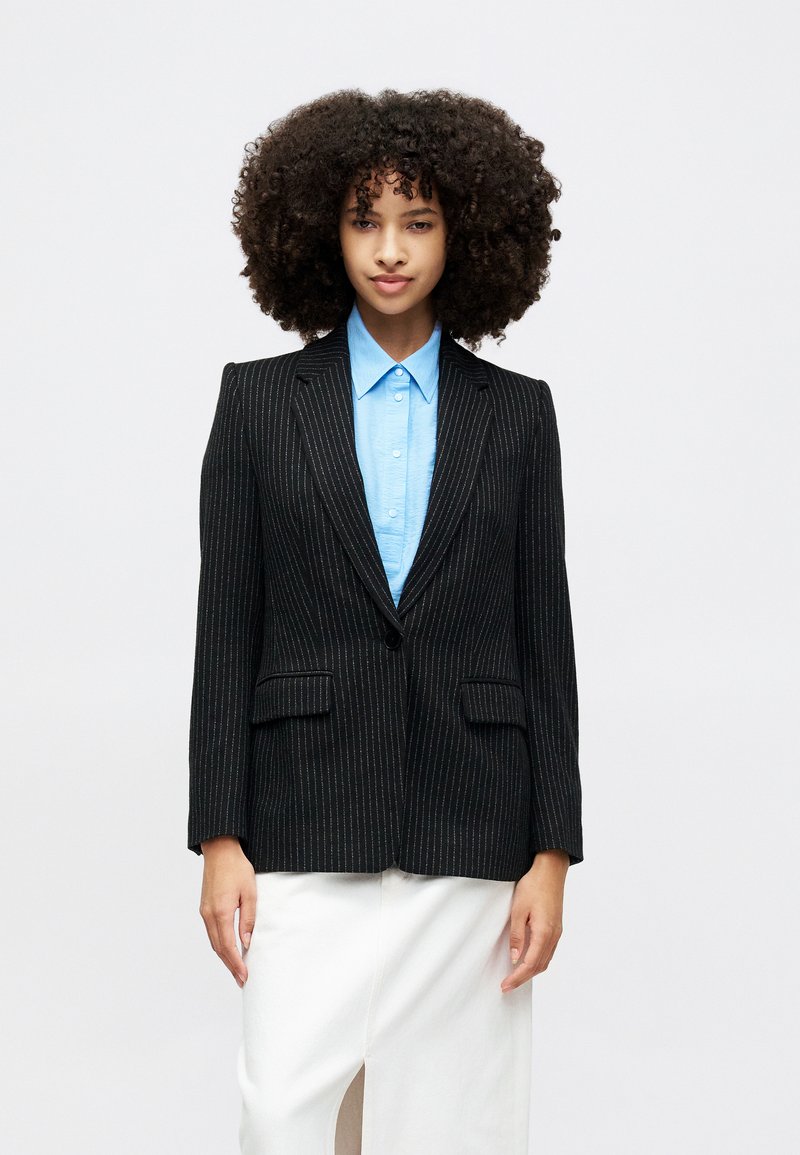 Czarna marynarka w paski z wykładanym kołnierzem, dwiema przednimi kieszeniami i pojedynczym zapięciem na guzik, noszona na jasnoniebieskiej koszuli.