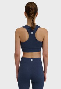 Marinblå sport-bh och leggings tillverkade av stretchmaterial, med racerback-design och subtila vita logodetaljer på ryggen.