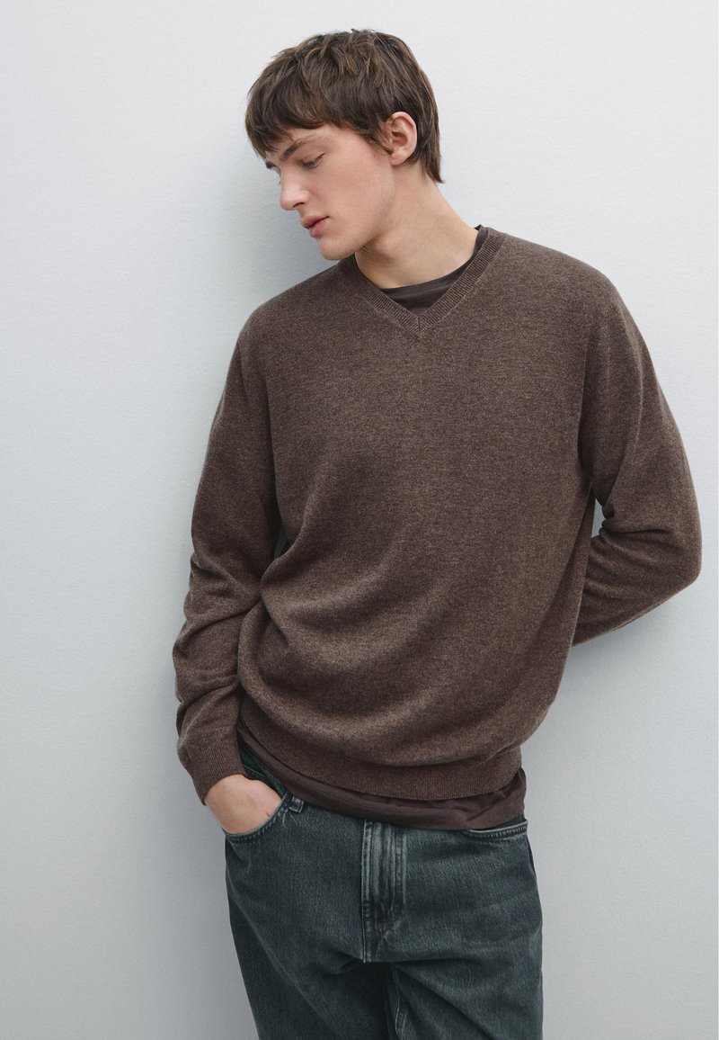 Brown v-neck sweater made of soft material, featuring a relaxed fit and long sleeves, paired with dark textured jeans.