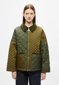 Πράσινο μπουφάν καπιτονέ με καφέ γιακά από κορδόνι, κλείσιμο με φερμουάρ και πλαϊνές τσέπες με λογότυπο. Υφασμάτινες επιφάνειες σε αντιθετικές αποχρώσεις.