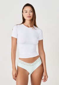 Top bianco a maniche corte abbinato a mutandine verde menta chiare con cintura in pizzo. Il tessuto appare liscio e aderente.