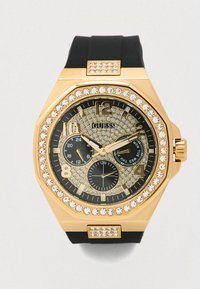 Orologio ottagonale dorato con cinturino in gomma nero, dettagli in cristallo, quadrante nero e tre sottoquadranti; caratterizzato da indici orari marcati e logo del marchio.