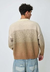 Pull en maille avec un col côtelé, présentant un dégradé de couleurs allant du crème au beige puis au marron, avec une surface texturée et des motifs subtils.