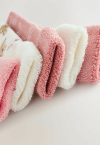 Paires de chaussettes en tissu éponge douces, en rose, blanc et motifs variés, disposées en rangée sur une surface blanche.