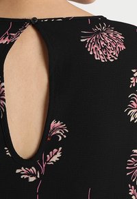 Schwarzes Stoffoberteil mit rosa Blumenmustern, mit einer runden Rückennaht und einer Knopfverschluss sowie einer strukturierten Oberfläche.