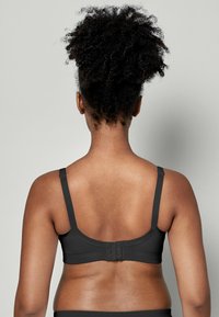 Schwarzer BH mit verstellbaren Trägern, nahtlosem Design und Haken- und Ösenverschluss auf der Rückseite. Glatte Stoffstruktur und körpernahe Passform.