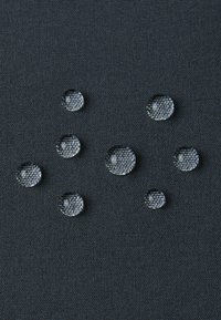 Des gouttes d'eau claires sur un tissu noir texturé créent un motif visuellement saisissant, soulignant le contraste entre les gouttes et l'arrière-plan.