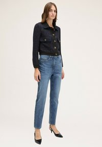 Chaqueta navy corta con dos bolsillos frontales y botones dorados; combinada con jeans rectos de color azul claro y tacones negros de punta. 