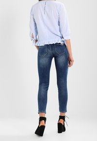 Blouse rayée bleu clair à manches trois-quarts et ourlet volanté, associée à un jean skinny bleu foncé et des bottes à chevilles noires.