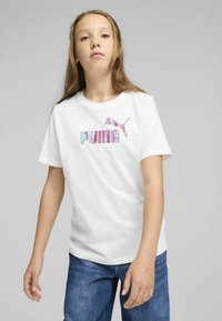 Camiseta de algodón blanca con mangas cortas, que presenta un logo de "PUMA" en degradado rosa y azul y un gráfico de un puma saltando en rosa en el pecho.