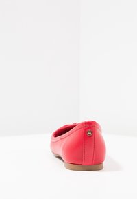 Ballet flat en cuir rouge avec un bout arrondi et un petit accent doré sur le talon. Texture lisse et design minimaliste.