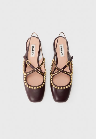 Scarpe slingback in pelle marrone con borchie dorate lungo il bordo, design della punta quadrata e cinturini incrociati. Etichetta del marchio visibile all'interno.
