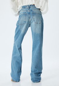Jeans in denim blu a vita alta con una vestibilità rilassata, dotati di tasche posteriori e una texture leggermente scolorita. Le gambe sono ampie e dritte.
