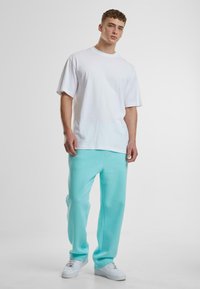 White cotton t-shirt paired with light teal sweatpants. Sweatpants feature a relaxed fit and are made from soft fabric, complemented by white sneakers.