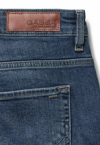 Tamsiai mėlynos džinsinės kelnės su šviesiai ruda odine etikete, pažymėta "GABBA", ant juosmens. Kelnės turi kontrastingą siuvinėjimą ir mažą firminę etiketę kišenėje.