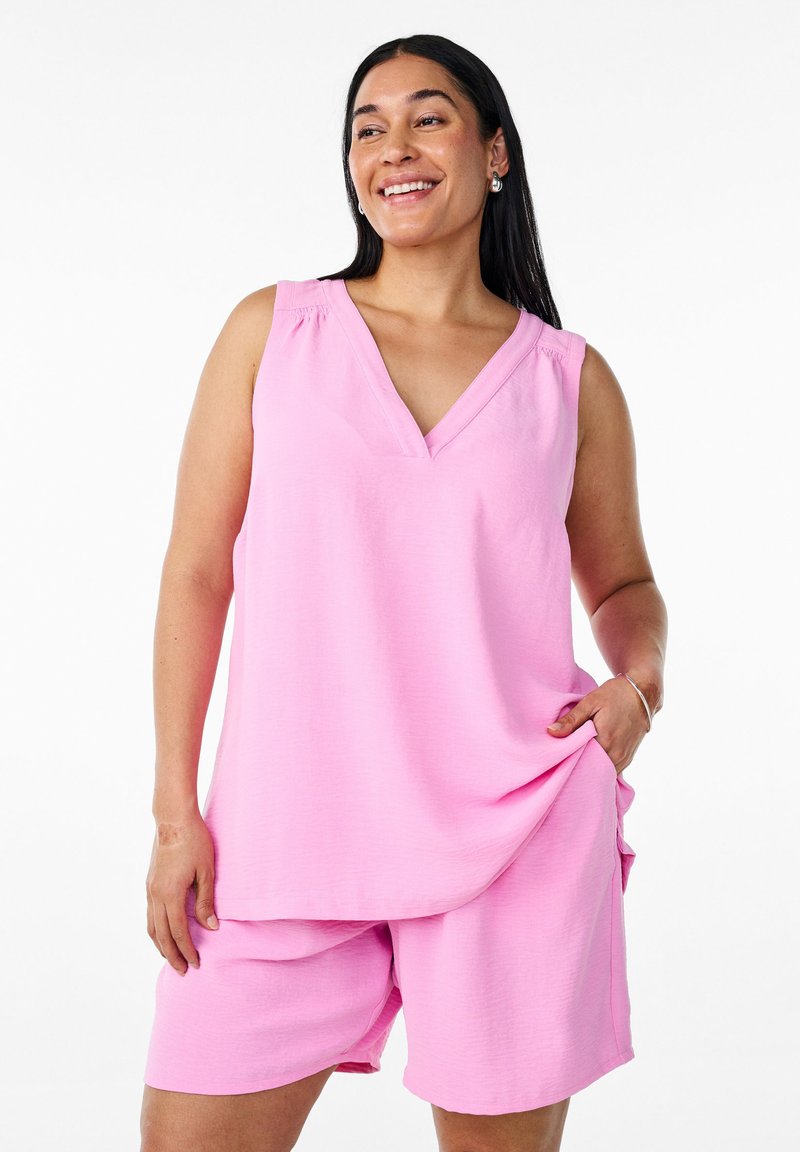 Top rosa senza maniche con scollatura a V e dettagli di arriccio discreti, abbinato a pantaloni corti rosa coordinati. Tessuto morbido, veste in modo casual.
