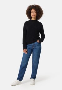 Svart, rundhalsad tröja med långa ärmar, tillverkad av mjukt material. Matchad med högmidjade blå jeans och vita sneakers.