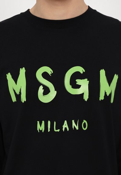 Svart langermet t-skjorte med fet, penselstrøkstil grønn tekst som sier "MSGM MILANO" over brystet. Myk stofftekstur.