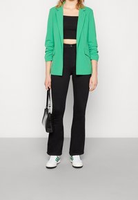Blazer verde, top corto negro, vaqueros acampanados negros, zapatillas blancas con rayas verdes y bolso negro. Tela lisa y ajuste entallado.