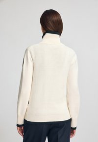 Crème-kleurige, gebreide trui met een hoge kraag en zwarte geribbelde accenten bij de kraag en de zoom. Heeft een relaxte pasvorm en lange mouwen.