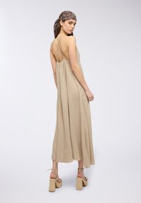 Abito maxi beige con spalline sottili, schiena scoperta e design arricciato. Indossato con sandali con tacco a blocco e cinturini. Foulard stampato leopardato.