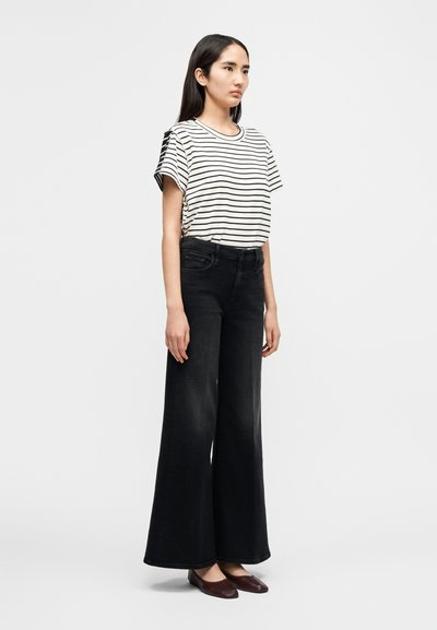 Ριγέ κοντομάνικο πουκάμισο σε κρέμ και μαύρο, σε συνδυασμό με φαρδιά μαύρα τζιν παντελόνια. Το σύνολο χαρακτηρίζεται από μ ινιμαλιστικό σχεδιασμό και επίπεδα παπούτσια.