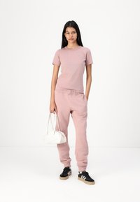 Camiseta de algodón rosa claro, joggers a juego y zapatillas negras. El modelo sostiene un pequeño bolso blanco. Estilo sencillo, fit relajado y casual.