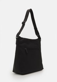 Borsa a spalla nera con tracolla regolabile e tasca anteriore con zip, in piedi su uno sfondo bianco uniforme.