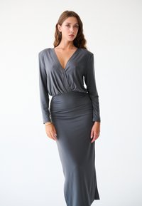 Robe grise à manches longues avec un décolleté en V profond et une taille froncée. Fabriquée en tissu lisse et extensible avec une silhouette ajustée et une fente sur le côté.
