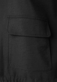 Schwarzer Stoff mit einer strukturierten Oberfläche, ausgestattet mit einer großen aufgenähten Tasche mit genähten Kanten. Schlichtes Design ohne zusätzliche Verzierungen.