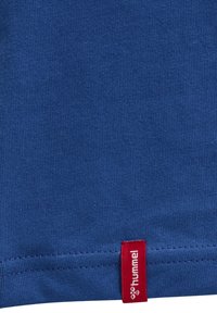 Blå bomullströja med en slät yta, korta ärmar och en röd etikett i fållen med "hummel"-logotyp.