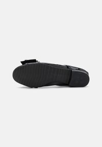 Sandale noire avec une semelle en caoutchouc texturé et un talon plat. Présente une finition mate et une seule sangle réglable sur le pied.