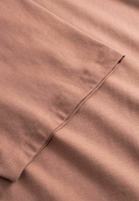 Tissu en coton brun clair présentant une texture lisse et des coutures visibles le long du bord, mettant en valeur un design doux et plié.