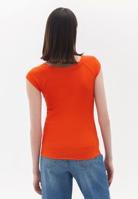 Top a maniche corte aderente in tessuto a costine arancione brillante, con scollatura rotonda e texture liscia, abbinato a jeans di denim blu chiaro.