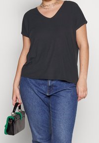 Maglietta a maniche corte grigia antracite con scollatura a V e vestibilità comoda, abbinata a jeans blu e a una piccola borsa nera con dettagli verdi.