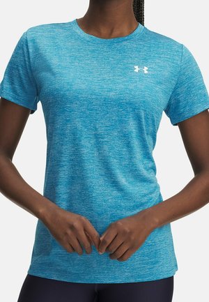 Persona dalla pelle scura che indossa una maglietta a maniche corte Under Armour blu sfumata, con le mani leggermente incrociate davanti.